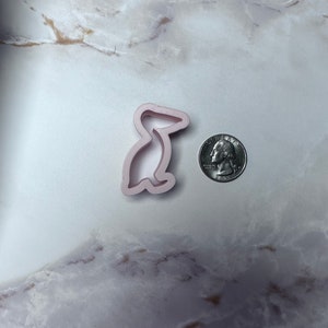May include: A pink plastic cookie cutter shaped like a pelican. The cutter is about the size of a quarter.