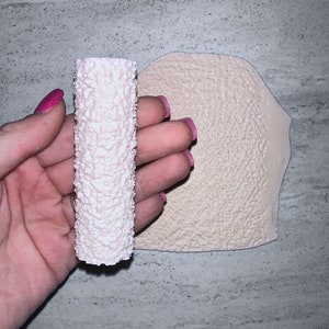 May include: A white textured roller and a flat sheet of white textured material. Both items are used for creating a textured effect on walls or other surfaces.