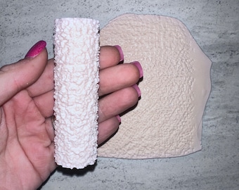 May include: A white textured roller and a flat sheet of white textured material. Both items are used for creating a textured effect on walls or other surfaces.