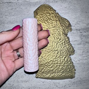 May include: A pink candle with a textured surface. The candle is in a cylindrical shape.