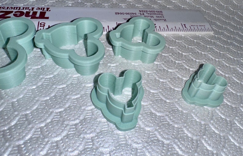 May include: Set of five green plastic cookie cutters shaped like Mickey Mouse heads. The cutters are different sizes.