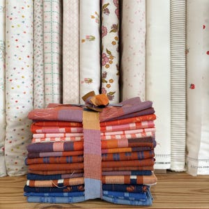 May include: A stack of folded fabric squares in various colours including purple, orange, pink, and blue, secured with a multicoloured fabric band. The stack is positioned in front of several vertical rolls of patterned fabric on a wooden shelf.