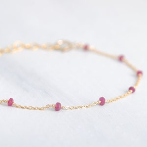 Op de afbeelding: Een delicate gouden kettingarmband met kleine, rode edelsteen kralen.