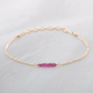 Op de afbeelding: Een delicate gouden kettingarmband met een rij kleine, roze robijnstenen in het midden.