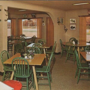 May include: An interior shot of a vintage restaurant with multiple tables and chairs. The tables are square or round, with green chairs. Large windows offer views of the outside scenery. The color palette is warm, with shades of brown and green.