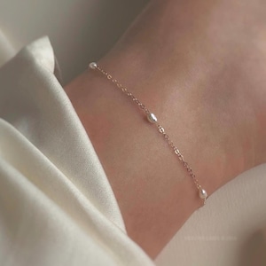 May include: A delicate gold chain anklet with small white pearls. The anklet is on a person's ankle.