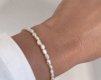 May include: A delicate pearl bracelet made of small, white, oval-shaped pearls. The bracelet is strung on a thin, silver chain.
