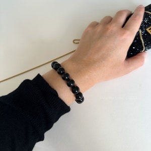 May include: A black beaded bracelet with round beads. The bracelet is worn on a person's wrist.