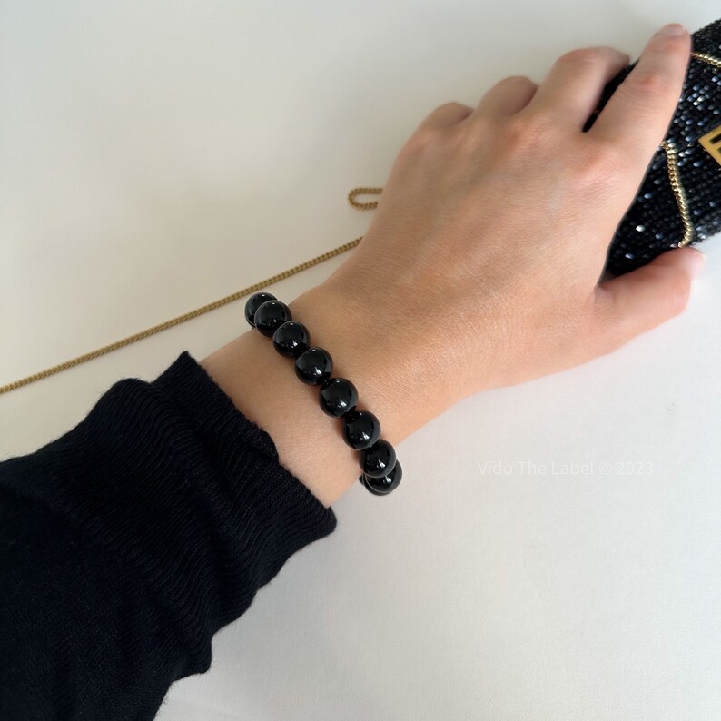 May include: A black beaded bracelet with round beads. The bracelet is worn on a person's wrist.
