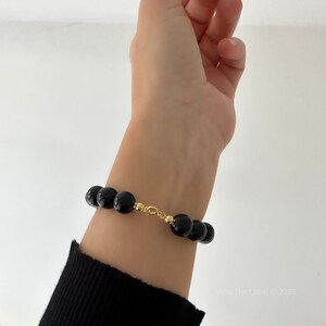 May include: A black beaded bracelet with a gold clasp. The bracelet is made of round, black beads and has a gold clasp.