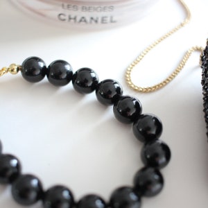 May include: A black beaded necklace with a gold chain. The necklace is made of large, round beads.