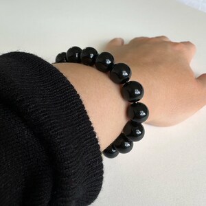 LARGE SHINEY BLACK BEADED BRACELET, MADE WITH 10MM OBSIDIAN BEADS.  LADY IS SHOWING IT WORN WITH A BLACK JUMPER