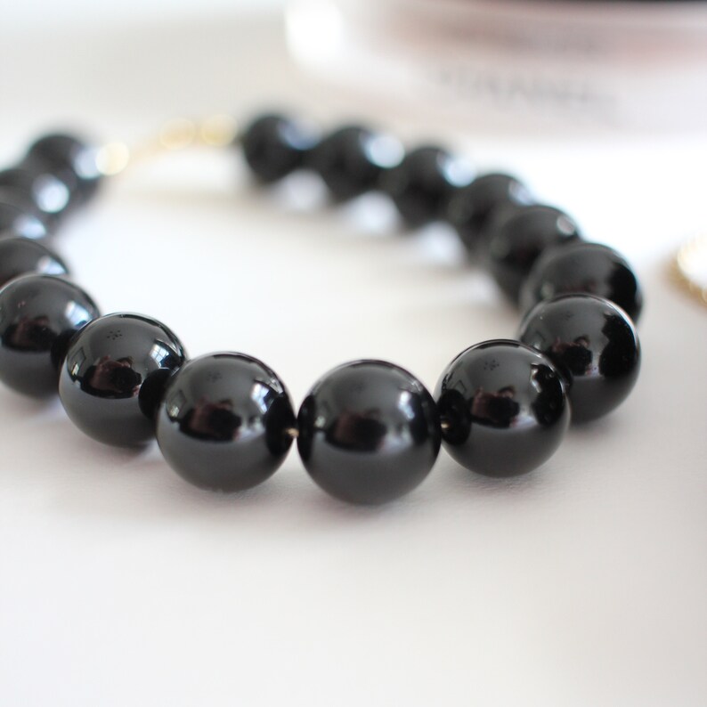 May include: A black beaded bracelet with a shiny finish. The bracelet is made of round beads that are strung together on a thin gold wire.