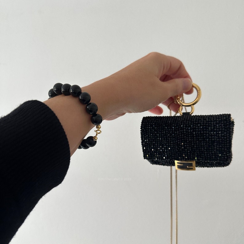 May include: A black beaded bracelet with a gold clasp and a small black sequined bag with a gold chain.