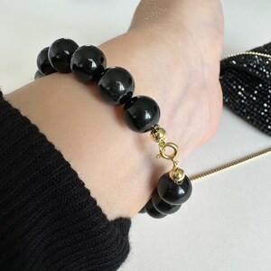 May include: A black beaded bracelet with a gold clasp. The bracelet is made of large, round beads and has a simple, elegant design.