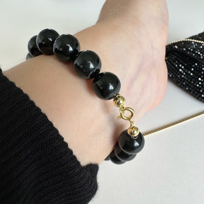 May include: A black beaded bracelet with a gold clasp. The bracelet is made of large, round beads and has a simple, elegant design.