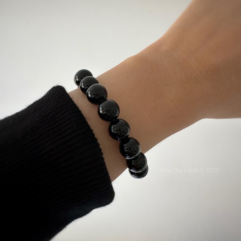 May include: A black beaded bracelet with round, smooth beads. The bracelet is worn on a person's wrist.