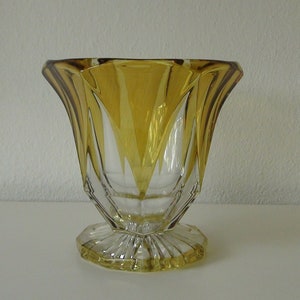 May include: A clear glass vase with a geometric design. The vase is amber coloured and has a wide, flared opening. The base of the vase is a clear glass with a fluted design.