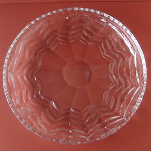 May include: A clear glass bowl with a decorative, starburst-like pattern on the inside. The bowl is empty and has a slightly rippled surface.
