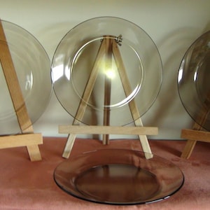 Può includere: Tre piatti in vetro trasparente su cavalletti di legno. I piatti sono rotondi e hanno un leggero bordo. I cavalletti sono in legno naturale e hanno un design semplice.