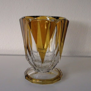 May include: A clear glass vase with a geometric design. The vase has a wide, flared mouth and a narrow base. The glass is amber-coloured and has a clear, crystalline appearance.