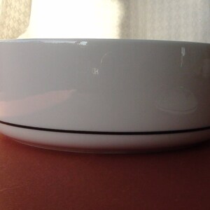 May include: A white ceramic bowl with a black rim. The bowl is round and has a smooth, glossy finish.