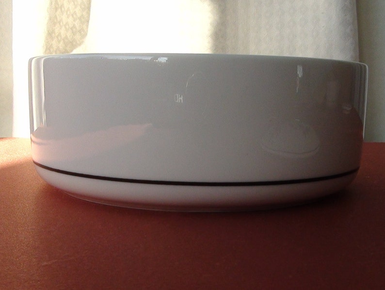 May include: A white ceramic bowl with a black rim. The bowl is round and has a smooth, glossy finish.