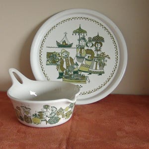 May include: A white ceramic serving tray with a green and brown design featuring a group of people with umbrellas and a boat. The tray is paired with a white ceramic bowl with a green and brown design featuring a fish and floral motifs.
