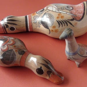 Può includere: Tre figurine di uccelli in ceramica dipinte a mano. Gli uccelli sono in tonalità di marrone, bianco e arancione con accenti neri. Gli uccelli sono tutti di dimensioni diverse e hanno pose diverse.