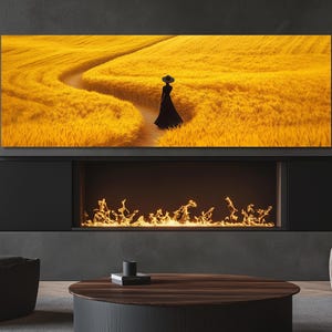 Könnte beinhalten: Ein großer rechteckiger Leinwanddruck zeigt eine Person in einem schwarzen Kleid und Hut auf einem Weg durch ein goldenes Weizenfeld. Das Kunstwerk ist über einem modernen Kamin mit dunkler Umrandung und Flammeneffekt montiert.