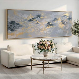 May include: A large rectangular wall art piece in a light wood frame featuring a landscape painting with grey, white, and gold tones. The artwork depicts stylized mountains, flowing rivers, clouds, and golden structures with dragon motifs.