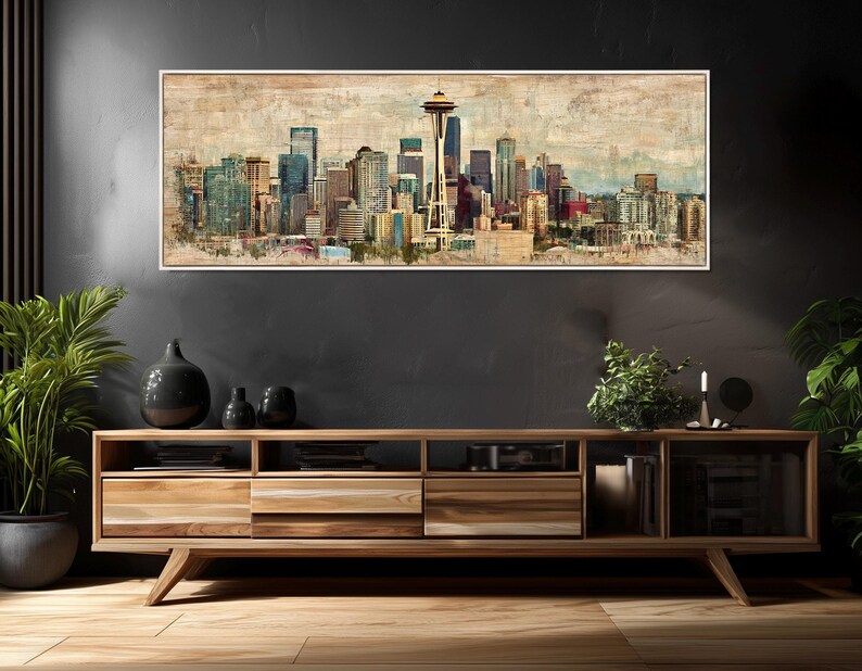 May include: A framed panoramic print of the Seattle skyline, featuring the Space Needle and various skyscrapers. The artwork has a vintage, textured appearance with muted colors, including blues, browns, and greens. The print is displayed above a wooden media console.