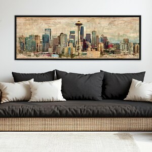 May include: A framed art print of the Seattle skyline, featuring the Space Needle and various buildings in shades of blue, brown, and gold. The artwork has a vintage, watercolor-like aesthetic, with a black frame.