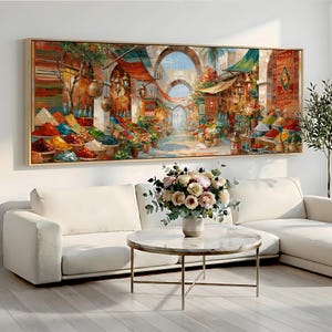 May include: A rectangular wall art print featuring a vibrant, detailed painting of a bustling outdoor market scene with colorful spice mounds, hanging lanterns, and stone archways, framed in a light-colored wood border and displayed on a wall.