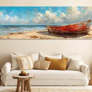 May include: A panoramic canvas print shows a distressed red boat on a sandy beach beneath a bright blue sky with fluffy white clouds. The ocean waves gently lap the shore, creating a tranquil coastal scene.