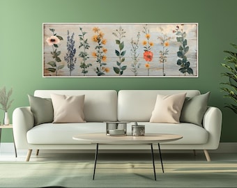 May include: A framed floral print featuring watercolor illustrations of various wildflowers in shades of pink, yellow, and purple. The artwork is set against a weathered wood background, creating a rustic aesthetic. The print is displayed above a white sofa.