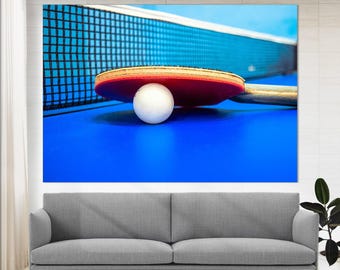 May include: A close-up of a red and black ping pong paddle and a white ball on a blue table tennis table. The table is surrounded by a black net.