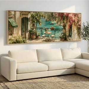 Könnte beinhalten: Ein rechteckiger Wandkunstdruck, der eine mediterrane Küstenszene mit einem Balkon über einem türkisfarbenen Meer zeigt. Das Gemälde enthält einen kleinen Tisch mit zwei Stühlen, einen Zitronenbaum, rosafarbene Bougainvilleen und eine grüne Markise.