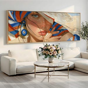 May include: A rectangular wall art print featuring a close-up portrait of a person wearing a wide-brimmed hat and a vibrant headscarf with bold orange, blue, and white stripes. The person has large blue eyes, coral lips, and a large circular earring.