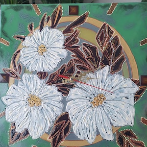May include: A green, gold and white clock with a floral design. The clock face is surrounded by three white flowers with gold centres. The background is a green circle with gold accents.