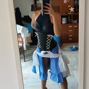 Może przedstawiać: Strój cosplay z czarnym topem na szyję z gorsetem ze sztucznej skóry i białym wzorem w stylu gorsetu. Strój zawiera niebieską spódnicę z białymi akcentami.