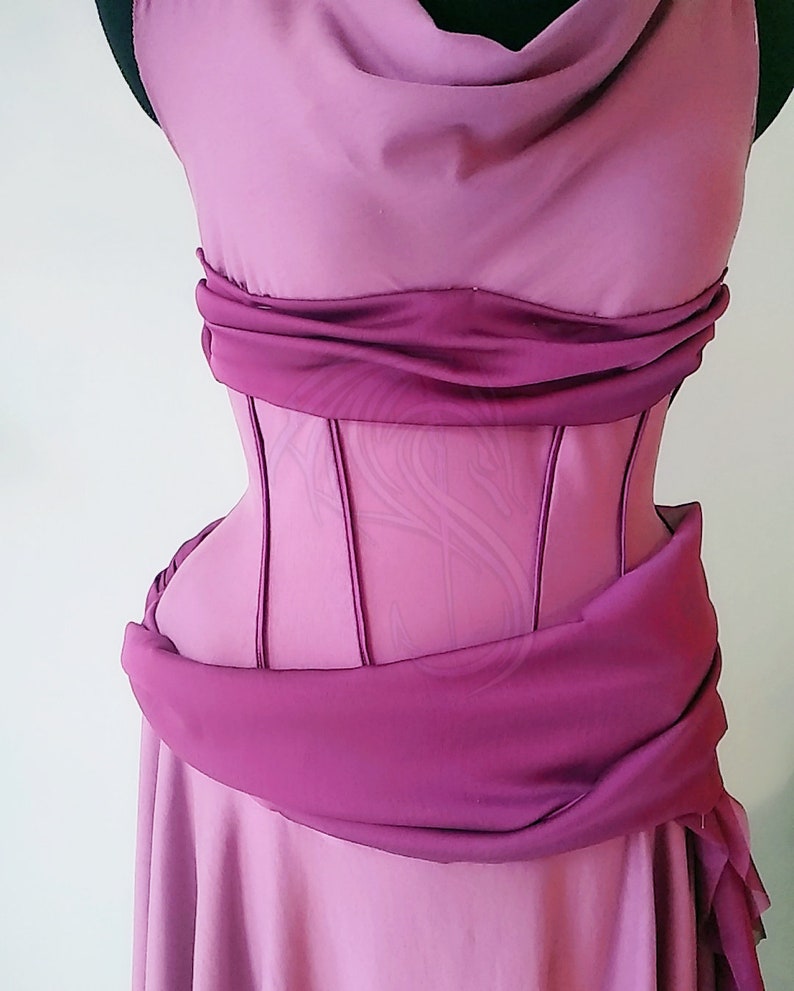 May include: A mauve dress featuring a structured corset-style bodice with vertical boning channels. The garment includes a draped cowl neckline and a wide, gathered fabric sash wrapped horizontally around the waist, creating a layered effect.
