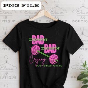 Peut inclure: T-shirt noir avec un graphique rose et vert d'une barre d'haltères avec le texte "Dad Down Dad Down Crying at the Gym".