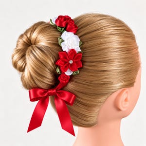 Puede incluir: Un accesorio para el cabello con una disposición vertical de rosas y pétalos de tela rojos y blancos, acentuados con hojas verdes y un brillante central. Una cinta larga de satén rojo está atada en un lazo en la base del conjunto floral.