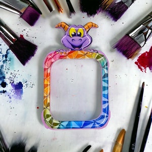 May include: A colorful phone case with a rainbow geometric design and a purple dragon character on the top. The case is made of hard plastic and has a clear back.