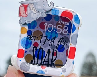 Puede incluir: Un Apple Watch blanco con un diseño de lunares de colores con un personaje de Dumbo el elefante. La esfera del reloj muestra la hora "10:58" y la fecha "FRI 25". La esfera del reloj también incluye el texto "don't just fly, soar".
