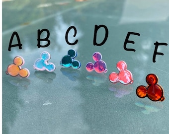Könnte beinhalten: Sechs schimmernde Mickey-Maus-Kopf-Anhänger in verschiedenen Farben: orange, rosa, blau, lila, rot und rot. Die Anhänger sind mit A bis F beschriftet.