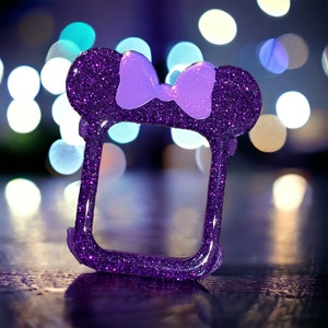 May include: Purple glitter phone case with a sparkly purple bow. The case has a cut-out for the camera and buttons.