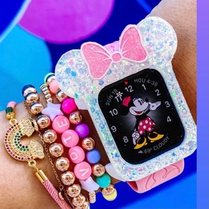 May include: A white glitter watch case with a pink bow and a Mickey Mouse watch face. The watch face shows the time as 4:36 and the date as Sun 18. The watch is on a wrist with several gold bracelets and colorful beaded bracelets.