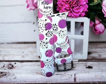 May include: White and pink patterned watch band with the text "We're all mad here" and a Cheshire Cat grin.